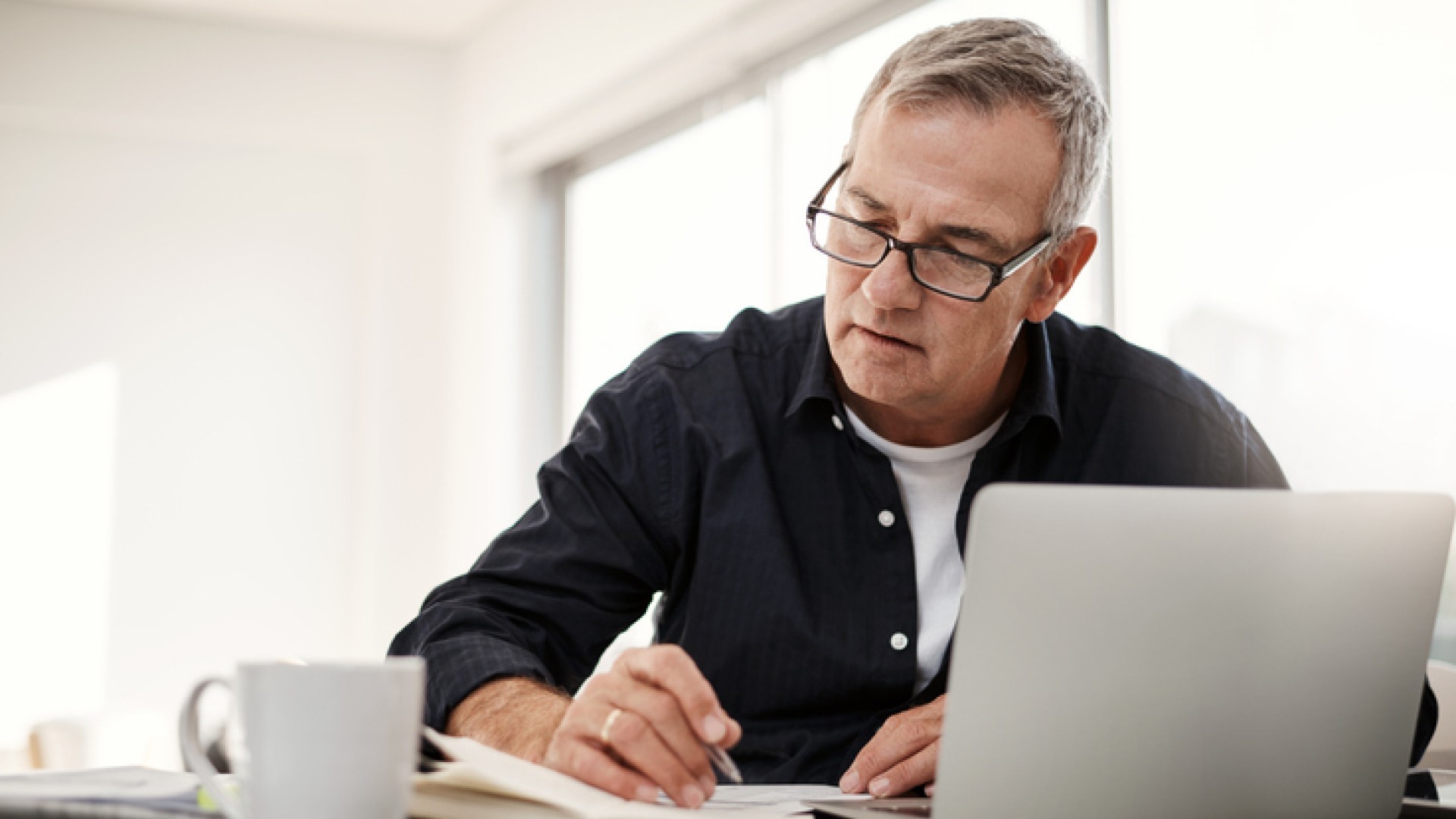 Man werkt geconcentreerd aan een bureau met een laptop en notitieboek.