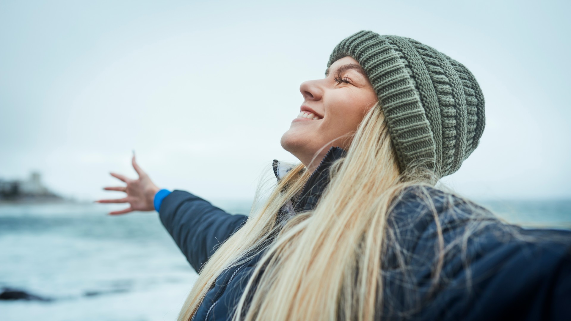 Vrouw geniet van de frisse lucht bij de zee met uitgestrekte armen.